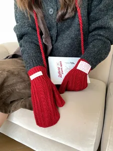 Detail of red cable-knit mittens with neck strap and white woven label on wrist