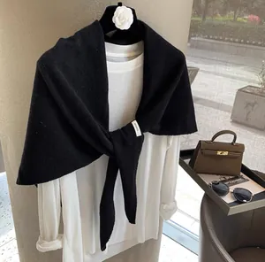 Detail shot of the 100% wool label on a black knitted shawl with a white shirt