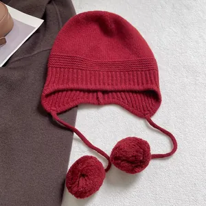 Detalle del gorro de lana con orejeras en rojo oscuro con grandes pompones decorativos