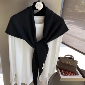 Detailed close-up of a black knitted shawl with a white logo label on the end