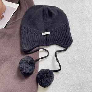 Detalle del gorro de punto de lana negra con pompones y etiqueta de material 100% lana