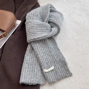 Detailed close-up of a grey ribbed wool knit scarf with a white rectangular brand label