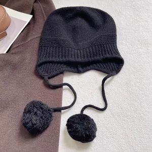 Textura detallada de un gorro de lana negro con orejeras y pompones suaves de piel