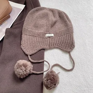 Detalle de gorro de punto 100% lana con orejeras suaves y pompones decorativos de felpa