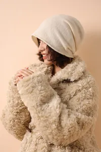 Dettaglio di un berretto in maglia bianco panna abbinato a un cappotto con alamari