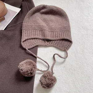 Primer plano de gorro de punto marrón oscuro con orejeras y pompones de lana suaves