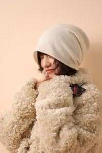 Dettaglio di un berretto in maglia bianco crema con un cappotto in pile e bottoni in corno
