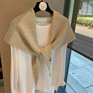 Detail of light beige knitted shawl with soft texture and brand label on a white top