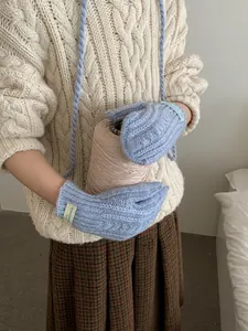 Detail of light blue cable knit gloves featuring a convenient neck strap and woven label