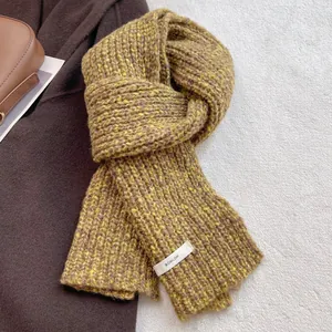 Close-up of mustard yellow chunky knit wool scarf texture with brand woven label