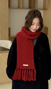 Detailed texture of red 100% wool cable knit scarf with fringes and material label
