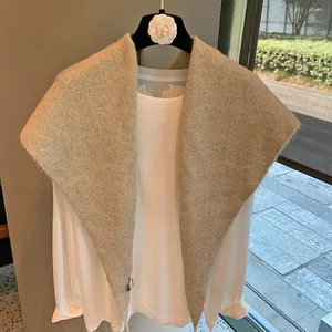 Close-up of oatmeal knit shawl over a white top on a decorative camellia hanger