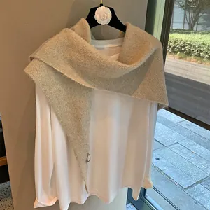 Detail of beige knit shawl texture with minimalist brand label on a white wooden hanger