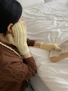 Detail of cable knit mittens in cream yellow featuring a neck strap and decorative tag