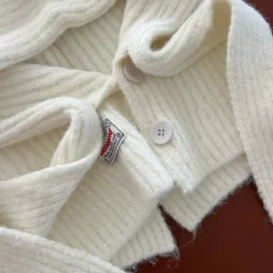 Detailed macro view of white ribbed knit cardigan with round buttons and fabric logo label