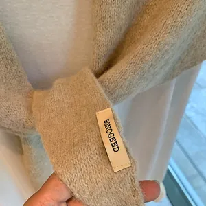 Close-up of beige knitted shawl featuring soft texture and black logo label detail