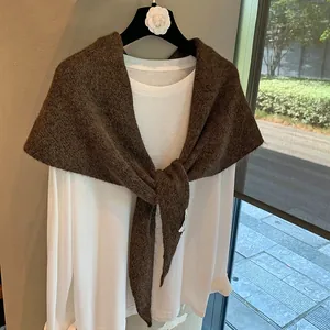 Detail of a brown knitted shawl tied over a white shirt showing thick textured fabric