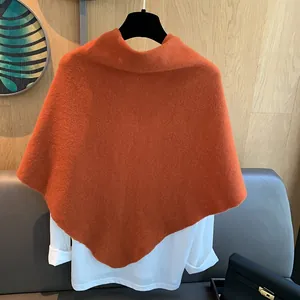 Detail of high-neck orange wool knitted shawl with asymmetric hem over white shirt