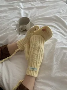 Detail of beige cable knit gloves with fingerless design and neck strap on white linen
