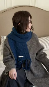 Detail of navy blue wool scarf featuring twisted knit patterns and long tassels on coat