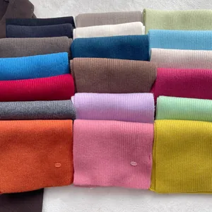 Flat lay of 100% wool ribbed scarves in 18 vibrant colors on soft grey plush background