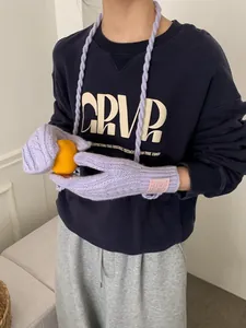 Detail of light purple cable knit gloves with hanging string on blue sweatshirt