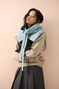 Détail de la cagoule en laine tricotée bleu clair portée sur un pull beige et une jupe plissée