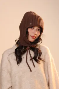 Dettaglio del cappello in maglia color caffè con paraorecchie e logo in metallo lucido