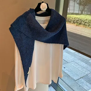 Detail of navy blue knitted shawl with plush texture draped over a white long sleeve top