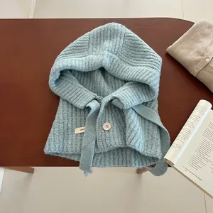 Cagoule tricotée bleu clair avec boutons en bois présentée sur un fond en bois rustique
