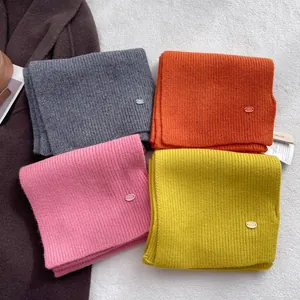 Knitted wool scarves in grey, orange, pink, and yellow with brand logo and tags