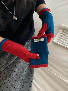 Detail of red and blue color-blocked knit half-finger gloves on a cozy white bed background