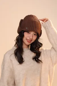 Dettaglio ravvicinato del cappello in maglia marrone scuro con paraorecchie e logo