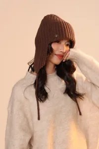 Dettaglio del cappello in maglia marrone scuro con paraorecchie e logo in metallo