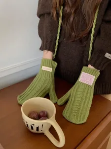 Detail of green chunky knit mittens showing the textured cable pattern and a fabric label