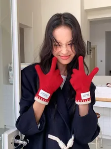 Close-up of red knit gloves featuring cream-colored cuffs and a Silent Wind woven label