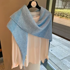 Close-up of light blue mohair knit shawl featuring fine texture and brand woven label