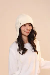 Dettaglio del cappello in maglia crema con paraorecchie, trama a coste e decoro argento