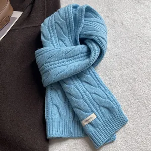 Détail de la maille torsadée bleu clair et étiquette de composition 100% laine sur l'écharpe