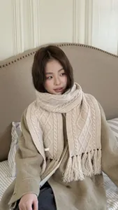 Close-up of beige cable knit wool scarf with decorative tassels and thick weave texture
