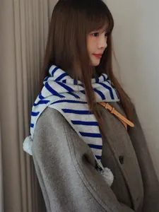 Detail of blue and grey striped knit scarf with soft plush pom-pom and ribbed texture