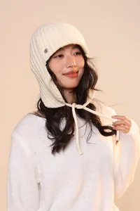 Dettaglio del cappello in maglia bianca con trama a righe verticali e lacci laterali