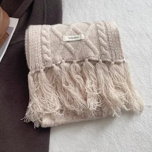 Detailed view of the 100% wool label and cable knit texture on a beige fringed scarf