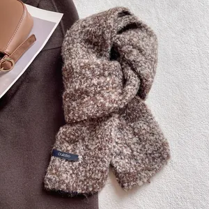 Dettaglio della sciarpa in lana bouclé marrone e beige con etichetta del marchio cucita