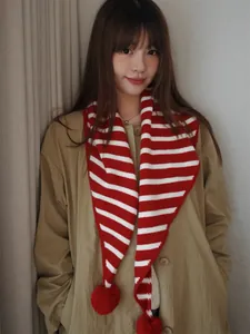 Detail of red and white striped knit scarf with decorative pom-poms on trench coat