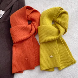 Detail of ribbed knit wool scarves in orange and yellow with metal logo plates