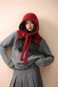 Détail d'une cagoule en laine tricotée rouge foncé avec bouton et cordons à nouer
