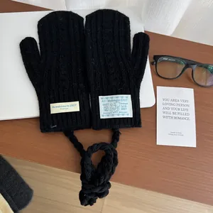 Detail of black cable-knit mittens with lanyard and decorative labels on a wooden desk