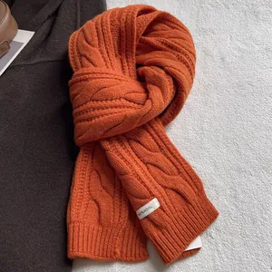 Gros plan d'une écharpe orange en pure laine avec maille torsadée et étiquette textile