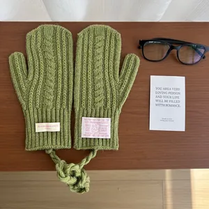 Detailed close-up of avocado green cable knit mittens with a neck strap on a wooden desk
